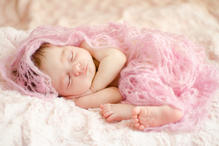 newborn sleeping baby girl wrapped in a knitted material, lying on soft fluffy rugの写真素材