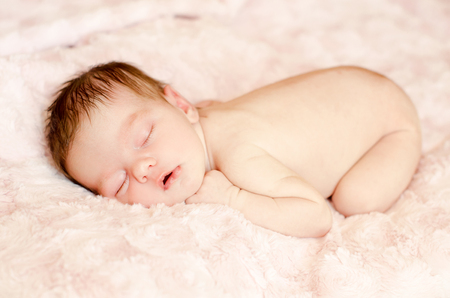 naked newborn baby sleeping on a soft fluffy rugの写真素材