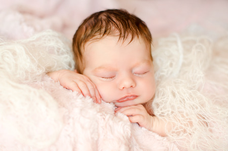 newborn sleeping baby girl wrapped in a knitted material, lying on soft fluffy rugの写真素材