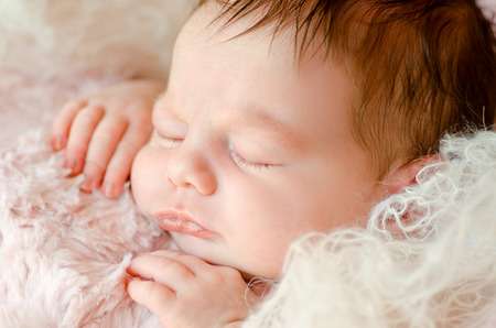 newborn baby close-up sleeping on a soft fluffy blankets, wrapped in knitted materialの写真素材