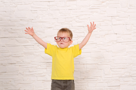 blond boy with glasses  and yellow shirt is spread out his hands against a white brick wallの写真素材