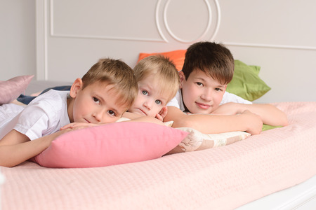 three boys lying on a bed of colorful pillowsの写真素材