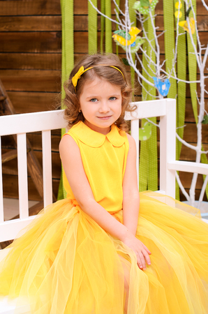girl in a yellow dress sitting on a white bench in the day of Easter Sundayの写真素材