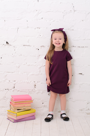 blond girl standing  near a pile of books in front of a white brick wallの写真素材