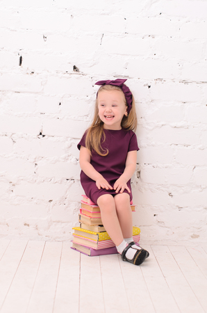 blond girl sitting on a pile of books against a white brick wallの写真素材