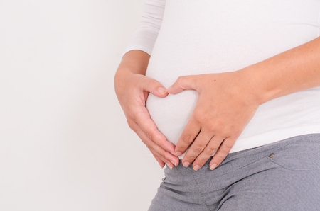 close-up of belly of a pregnant woman tenderly holding hands in the form of heart on a completely white backgroundの写真素材