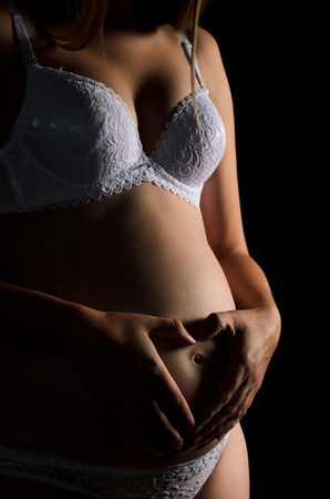 close-up of pregnant woman's belly, his hands on his stomach in the form of heart on a completely black backgroundの写真素材