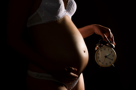 closeup of a naked pregnant woman's belly, one hand holding his stomach, dugaya - hours on a completely black backgroundの写真素材