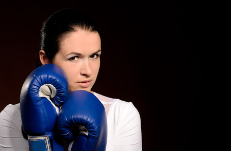 Girl in boxing gloves covers face protection pose against a dark background