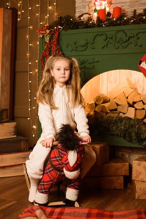 Girl riding toy horse near festive Christmas fireplaceの写真素材