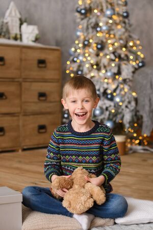 boy in sweaters, sitting on wooden floor, in room with Christmas tree, plaing to toy bearの写真素材