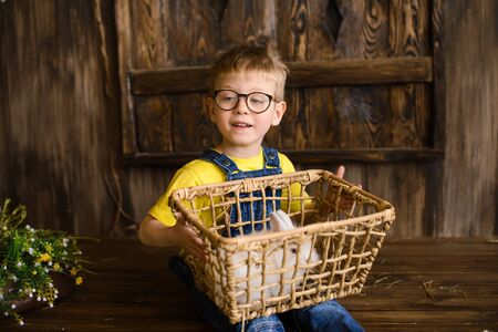 little boy in yellow T-shirt against background of wooden porch plays with white fluffy rabbitの写真素材