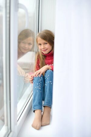 girl sits on windowsill, near windowpane, she wants to walk on street, but in  world there is coronavirus pandemic, and she remains at home in quarantineの写真素材