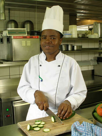 Black female chef is cutting zucchini on the cutting boardの写真素材