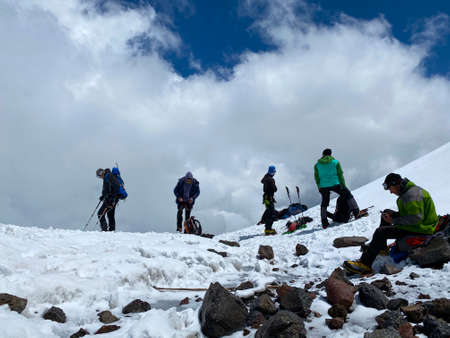 ELBRUS DISTRICT, RUSSIA - JULY 7, 2020: A group of climbers with backpacks and trekking poles stands and rests on a snowy trail. Snowy slopes of the northern Elbrus region. Mountain winter landscape.のeditorial素材