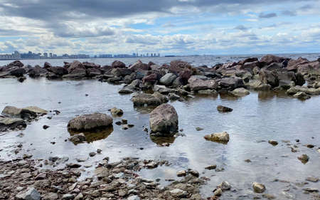 Rocky seashore with a city in the distance. Beautiful sea with small waves. The waves beat against the stones.の写真素材