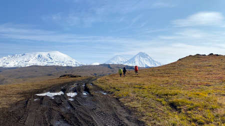 Three tourists with big backpacks and trekking poles go to the volcanoes of Kamchatka. Trekking in the Klyuchevskoy volcano park. Travel to the Kamchatka Peninsula.の写真素材