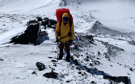Climber in a yellow jacket with an ice ax goes to the top of the volcano along a snow-covered trail. Mountain climbing. Trekking in the Klyuchevskoy volcano park. Travel to the Kamchatka Peninsula.の写真素材