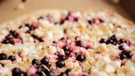 Large round sweet pizza pie with apple pieces, berries, almond slices and condensed milk in a cardboard box. Male hands take two slices of sweet pizza. Close-up.の写真素材