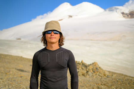 Portrait of a young male climber in mountain sunglasses against the background of Mount Kazbek....