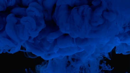 Blue cloud of ink. Cosmic magic background. Waves and drops of blue paint. Beautiful abstract background. Blue watercolor ink in water on a black background.の写真素材