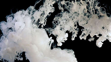 Drops of white ink in water. White abstract background. White watercolor ink in water on a black background.の写真素材
