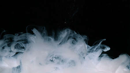 White watercolor ink in water on a black background. Waves of milky ink and splashes of white paints...