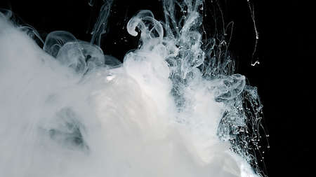 White watercolor ink in water on a black background. Abstract background. Waves of milky ink and splashes of white paints in the water. White cloud of ink on a black background.の写真素材
