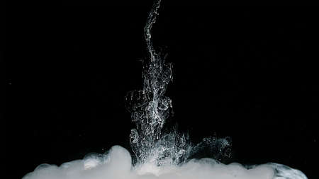 White watercolor ink in water on a black background. Waves of milky ink and splashes of white paints...