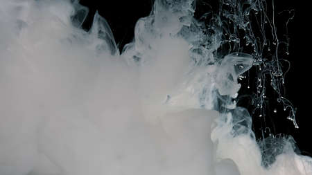 White watercolor ink in water on a black background. Abstract background. White cloud of milky ink....