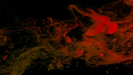 Orange ink droplets in water. Cosmic star background. Orange watercolor paints in water on a black...