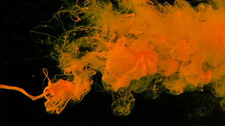 Yellow cloud of ink on a black background. Awesome abstract background. Colored ink cloud on gray background. Yellow watercolor paints in water on a black background. Desktop wallpaper.の写真素材