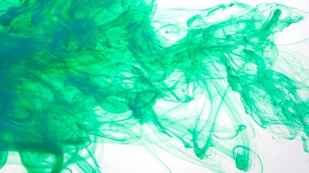 Colored cloud of ink on a white background. Blue-green watercolor ink in water on a white background. Beautiful abstract background. Green paints are mixed in water.の写真素材