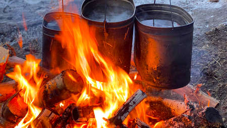 Close-up of iron pots of water over a large fire. Travel kitchen. Yellow-orange flames. Burning...