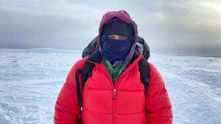 Survival in the north. A man in warm clothes with a backpack behind his back looks at the camera....