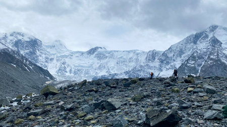 Two climbers with large backpacks are walking on the rocks. Climbing Mount Belukha. Beautiful mountain winter landscape. Amazing natural background. Altai Mountains. View of the Akkema wall.の写真素材