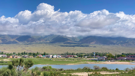 Beautiful summer mountain landscape. View of the mountain range with a small town in the valley below. Travel to Kyrgyzstan. The sky is overcast and the sun is not visibleの写真素材