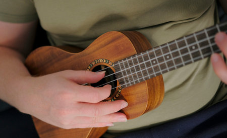 The guy plays the ukulele, top view. A musician gives ukulele lessons, a close-up of a hand plucking strings. A man is playing a small guitar. The guitarist is wearing a green shirt.の写真素材