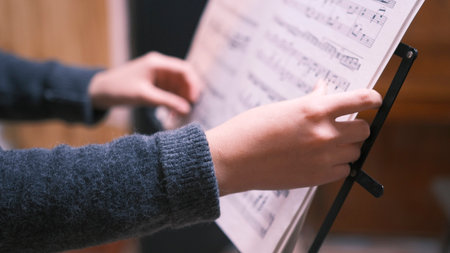 A young female musician holds a music notebook. A piano student holds notes in his hands and looks...