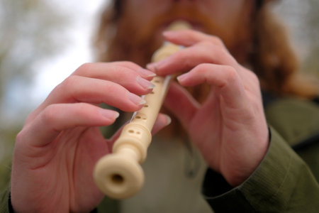 Close-up of a red-haired bearded man playing a flute, focus on his hand. A piper learns to play the...