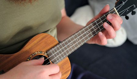 Ukulele lessons. The guy plays the ukulele, close-up, focus on the hand and strings. A musician in search of a new melody. Creativity and inspirationの写真素材