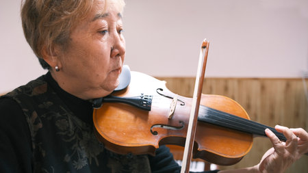 An old Asian woman plays the violin, close-up. Violin lessons. An elderly teacher shows how to play the violin correctly. A focused musician. Music Schoolの写真素材