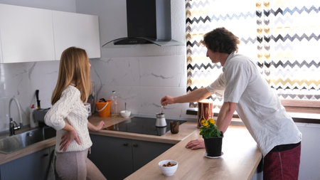 A young couple is making coffee in the kitchen. A man and a woman are standing in the kitchen. Waiting for breakfastの写真素材