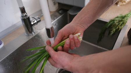 A vegetarian person washes Scallions in the kitchen sink, close-up. The person cooks themselves a lunch of fresh natural vegetables. Proper nutritionの写真素材