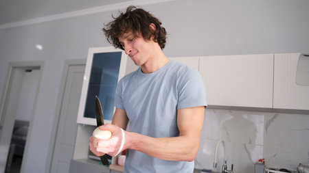 A handsome man cuts white onions in the kitchen while dancing. Cooking a vegetable dish....