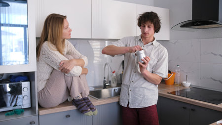 Morning young family. A man washes a Turk while talking to his girlfriend in the kitchen. Making morning coffee. A woman is sitting on the kitchen tableの写真素材