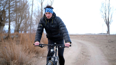 A sporty guy attentively rides a bike through the countryside. Bike training. He is wearing a black...