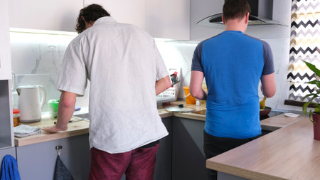 A back view of a gay couple cooking a delicious dinner. Two men are in the kitchen, one of them is...