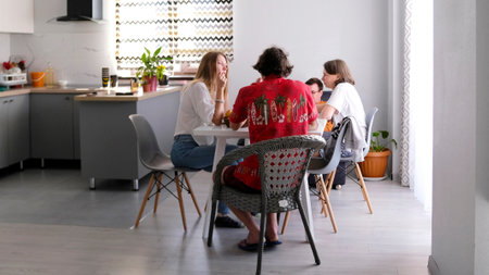 A group of young men and women are sitting at a table in the kitchen. Four friends rent a large apartment. Youth lifeの写真素材