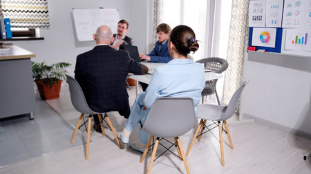 Colleagues are going to a briefing in the meeting room. A group of people is sitting at a table in a...